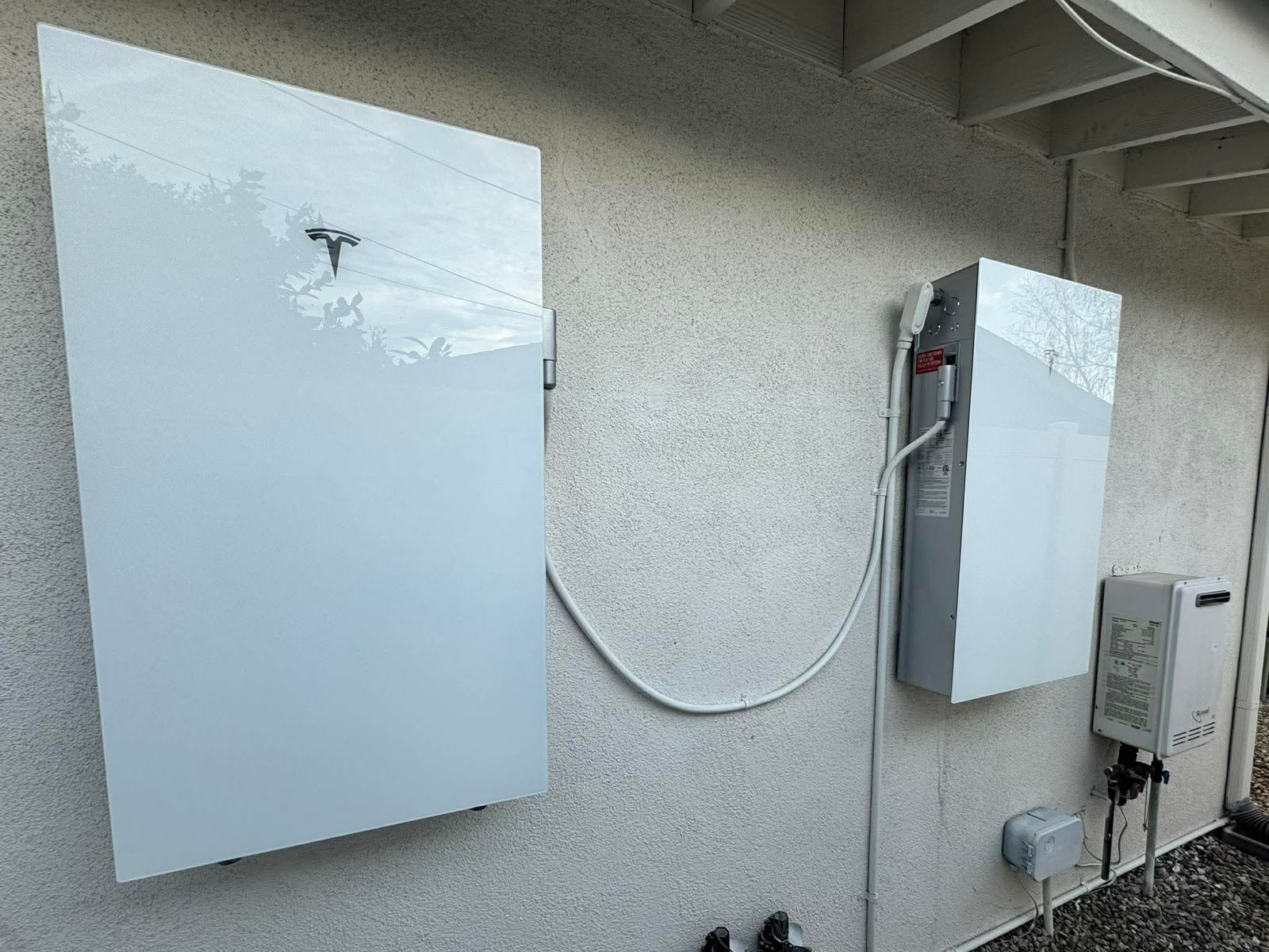 Tesla Powerwall home battery and backup gateway installed on the side of a stucco home