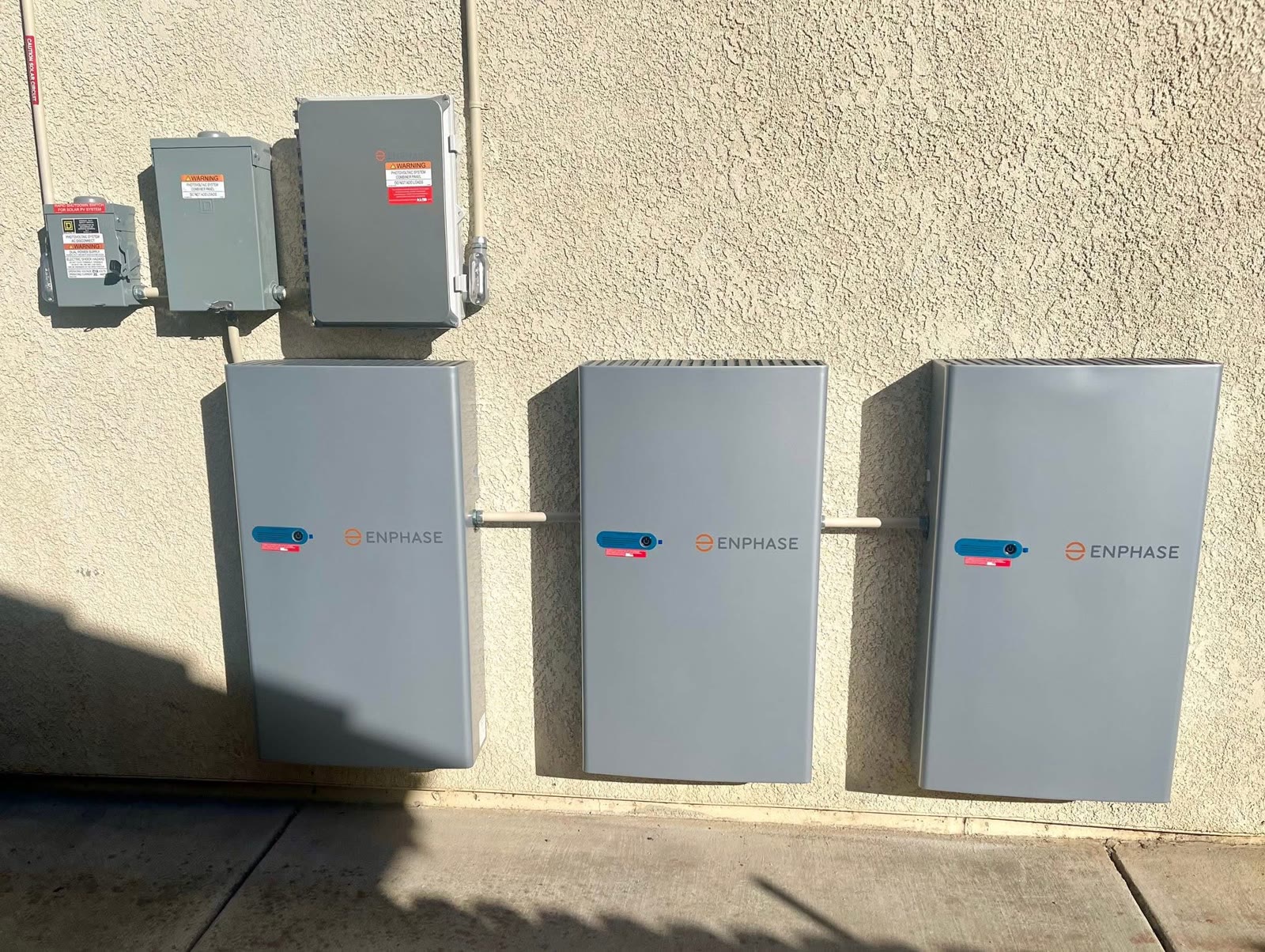 Three Enphase home battery units installed on an exterior wall