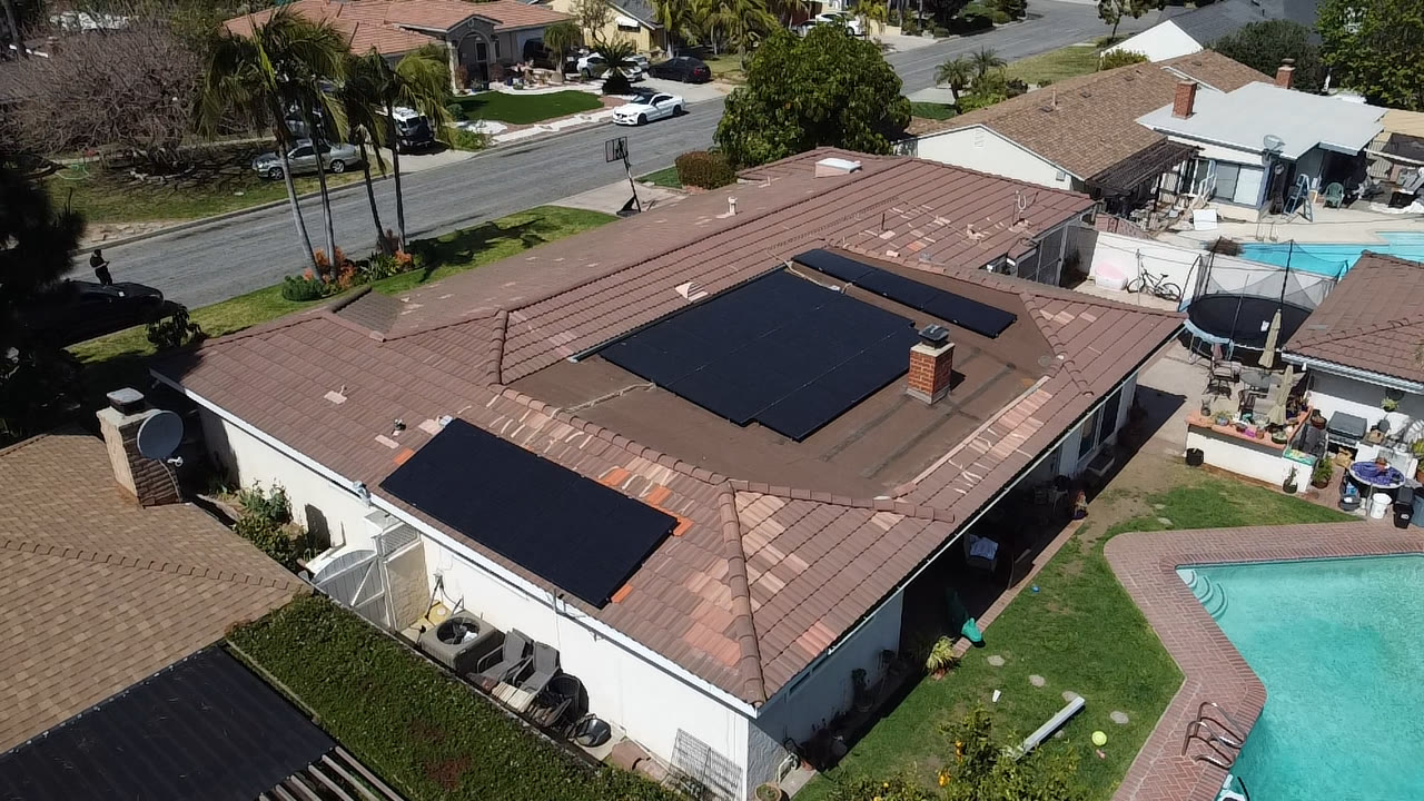 Aerial view of a tile-roof home with solar panels and a backyard pool